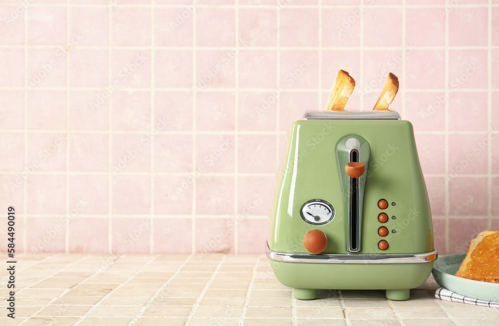 Modern toaster with crispy bread slices on tile table