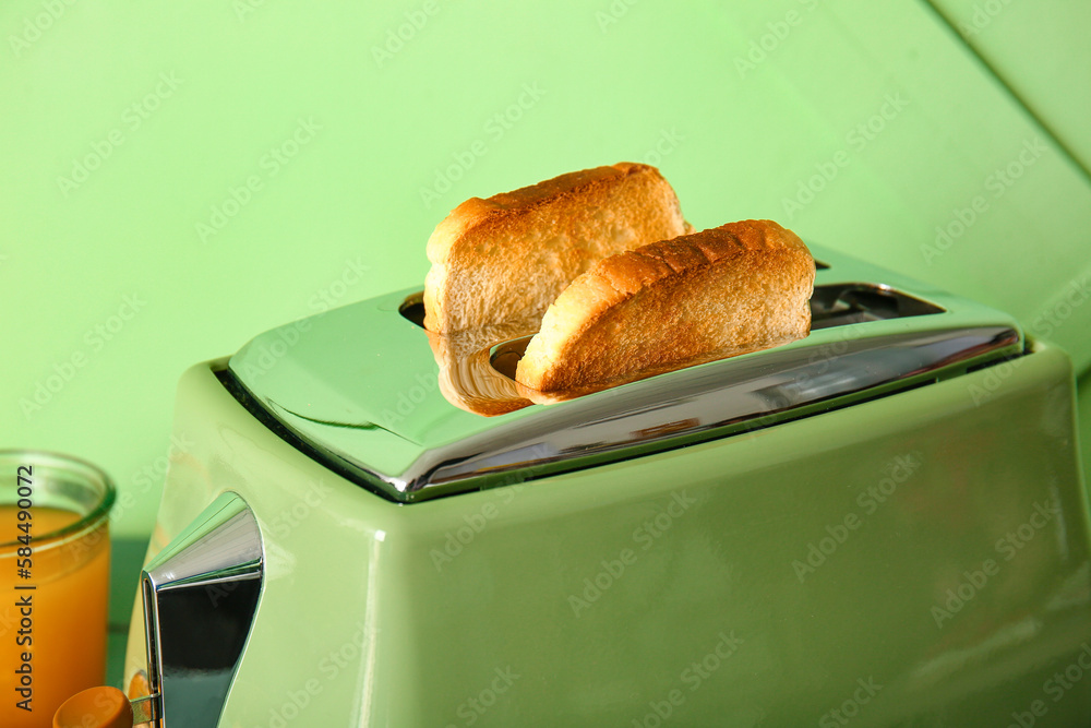 Crispy bread slices in modern toaster on green background, closeup