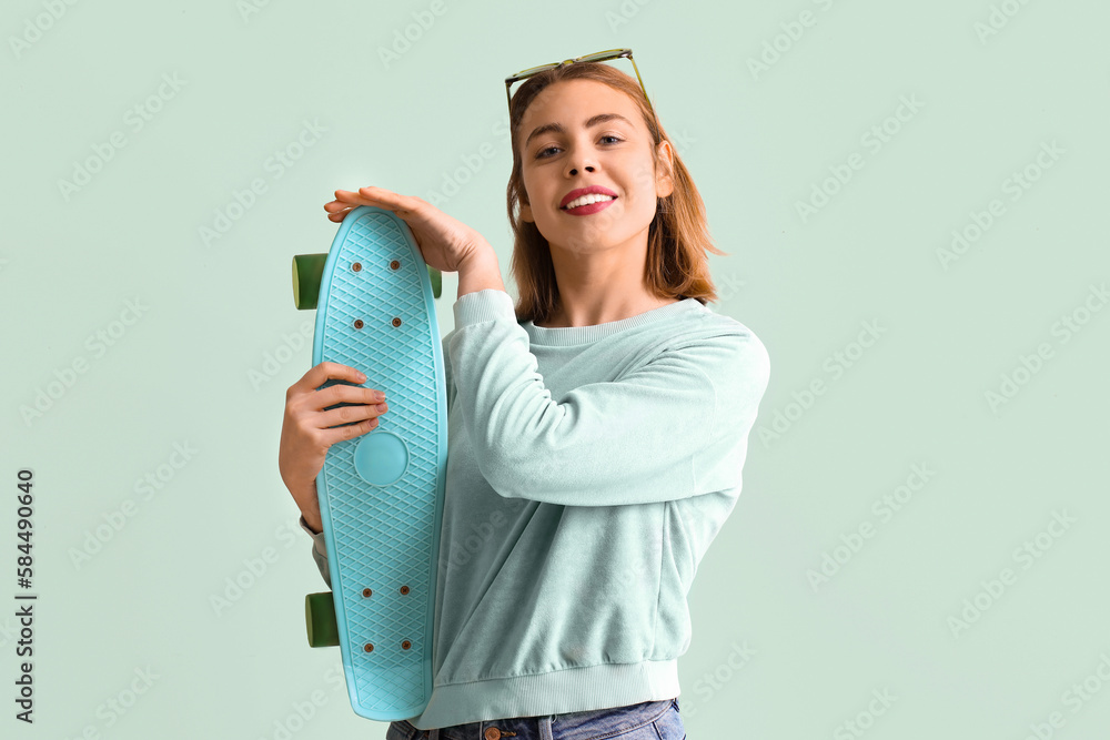 Young woman with skateboard on green background
