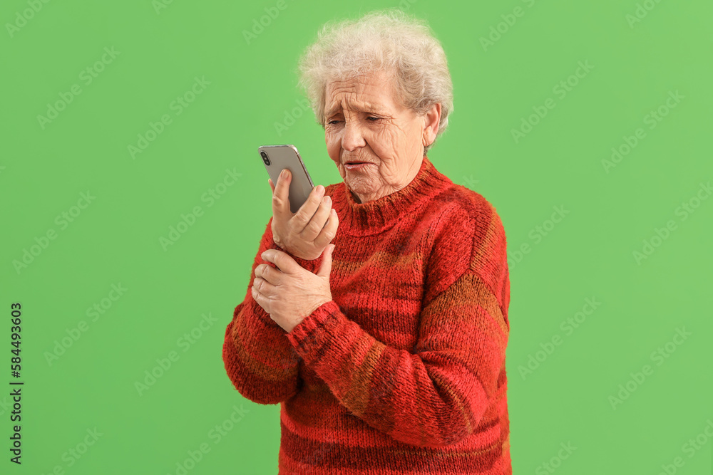 Sad senior woman with mobile phone on green background