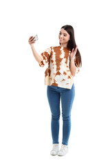 Wall Mural - Stylish young woman in tie-dye t-shirt taking selfie on white background