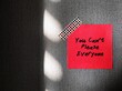 Red note stick on wallpaper with handwritten text You Can’t Please Everyone - self reminder to stop trying to please everyone and be your authentic self