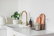Beautiful bright interior of the kitchen in a minimalist style - kitchen furniture with ceramic sink, brass faucet, cutting boards, kettle and homemade flower on the surface
