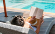 © Pattarisara - Happy girl lying down on sunbed while reading a book near Swimming Pool on travel holidays vacation, wellness Lifestyle concept. Young Asian woman relaxing at hotel on weekend. Copy space