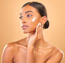 Sticker - Face, beauty skincare and woman with cream in studio isolated on a brown background. Dermatology, cosmetics idea and thinking Indian female model with lotion, creme or moisturizer for skin health.