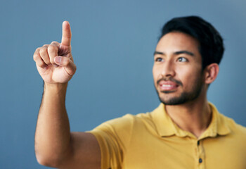 Canvas Print - Finger, pointing and asian man with invisible hologram in studio with mockup against blue background. Interface, hand and creative male entrepreneur with advertising, marketing or idea while isolated