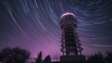A Stunning Photo Of The Purple It Tower, Lit Up Against The Night Sky, With Star Trails Above. Rotating Starry Sky
