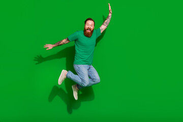 Wall Mural - Full size photo of handsome groomed childish man wear trendy t-shirt jeans jumping flying having fun isolated on green color background