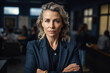 © nenetus - Confident executive woman posing in front of the camera with her arms crossed, behind her colleagues working in a modern office. Generative AI