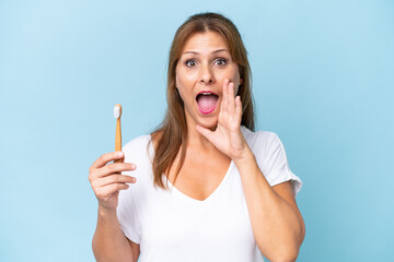 Canvas Print - Middle-aged caucasian woman brushing teeth isolated on blue background shouting with mouth wide open