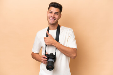 Wall Mural - Young photographer caucasian man isolated on beige background giving a thumbs up gesture