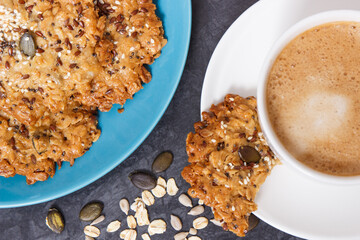 Cup of white coffee and fresh baked oatmeal cookies with honey and healthy seeds. Delicious crunchy dessert