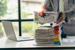 © ArLawKa - Asian office worker sitting at his desk clearing a lot of papers on the table at the office, OT concept