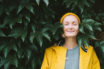 Portrait of relaxed and confident woman with eyes closed on background of green leaves wall. Thoughtful person in front of green hedge. Joy, zen and balance people. Stability through mental health