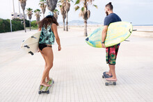 Young Couple Skating With Surfs To The Beach.