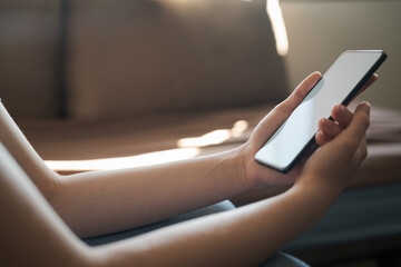 Wall Mural - Young woman hold smartphone with white screen while sitting on a couch