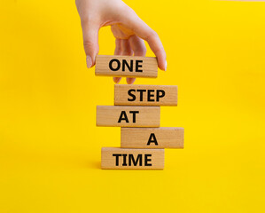 Wall Mural - One step at a time symbol. Concept words One step at a time on wooden blocks. Beautiful yellow background. Businessman hand. Business and One step at a time concept. Copy space.