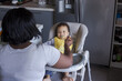 © Anna Berkut/Stocksy - mother feeding baby in high chair at home