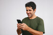© juanpablo - Middle-aged latin man with a smile using his smartphone on a white background.
