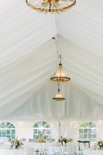 White Tent Filled With Tables And Chandeliers For Wedding Reception
