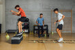 © BASILICOSTUDIO STOCK - Full length of Teenagers and personal trainer performing circuit routine training at gym. Male coach instructor and Two boys jumping running in a big gym with concrete wall. Horizontal
