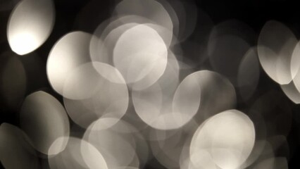 Wall Mural - Smooth circular motion of silver bokeh on black background. Slowly moving and shimmering movement of defocused circles. Abstract moving background with silver shimmering lights on bokeh lights.