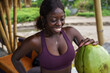 © Jovo Jovanovic/Stocksy - Happy woman in sports bra drinking coconut water at beach