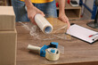 © New Africa - Post office worker wrapping parcel in stretch film at counter indoors, closeup