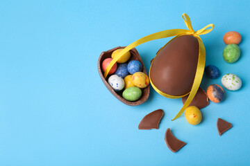 Wall Mural - Tasty whole chocolate egg with yellow bow and different candies on light blue background, flat lay. Space for text