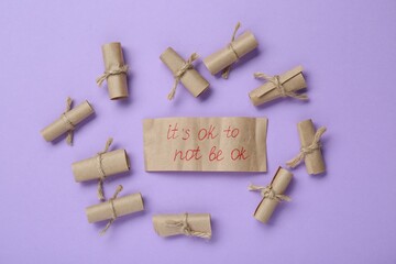 Wall Mural - Card with phrase It`s Ok to Not Be Ok and rolled pieces of paper on violet background, flat lay