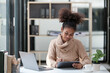© Treerat - American African Woman working in the office with computer phone and Tablet.