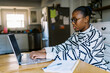 © Serena Burroughs/Stocksy - Black girl at home at kitchen table doing homework with laptop
