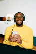 © Artem Podrez/Stocksy - A black man in a yellow sweater listens to music with headphones