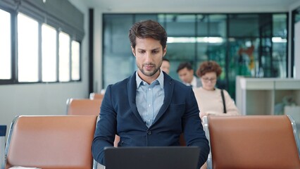 Handsome Indian or latin businessman sitting and working on laptop waiting for flight at airport terminal