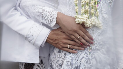 Wall Mural - couple gently holding hands in bridal attire. bridal hands with elegant wedding rings with white gold diamonds. Bride's hands close-up of a ring. High quality photos.