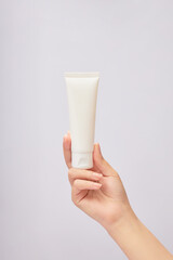 Female hand model holding an empty label white tube over white background. Concept of beauty products cream