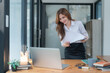 © Songsak C - Portrait of young Asian woman reading a document while standing at office desk.