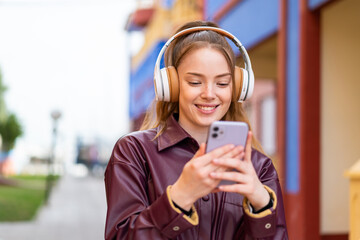 Young pretty girl at outdoors listening music and looking to mobile