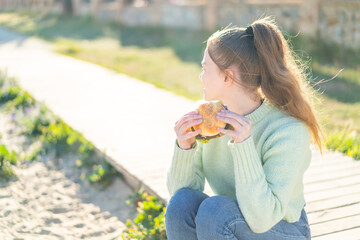 Sticker - Young pretty girl holding a burger at outdoors in back position