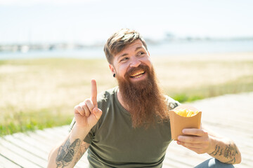 Wall Mural - Redhead man with beard holding fried chips at outdoors intending to realizes the solution while lifting a finger up