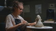 European blonde girl sculptor creates sculpture, statue for interior, bozzetto. The woman has her own local business, a freelancer. The female uses the tools of a sculptor, stecca for clay.