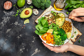 Wall Mural - Girl holding plate with hands vegan breakfast. meal in bowl with avocado, mushrooms, broccoli, spinach, chickpeas, pumpkin. top view