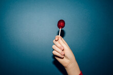 Hand Holding Red Lollipop Agains Blue Background 