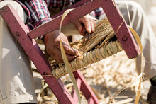 Artisan Finishes Cutting The Excess Of Dry Reed From A Chair