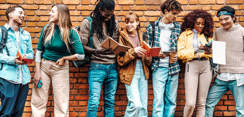 Happy young university students study with books leaning the wall out the campus - Group of youth multiracial people showing test results outside college - Multiethnic friends doing homework in school