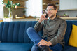 © Ivan - Handsome young man talking on smart phone and smiling while sitting on the sofa