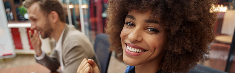 Wall Mural - Smiling african businesswoman sitting on his workplace in modern office on colleague background