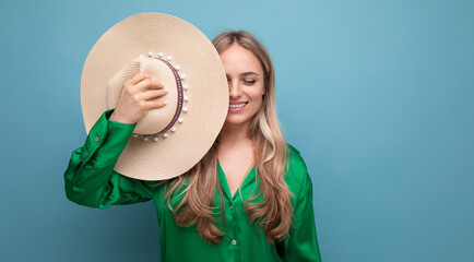 horizontal photo of a charming woman on vacation holding a straw hat near her face on a blue studio background