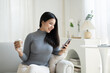 © PaeGAG - Young attractive Asian female using smartphone while sitting on the sofa in living room.
