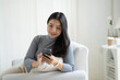 © PaeGAG - Young attractive Asian female using smartphone while sitting on the sofa in living room.